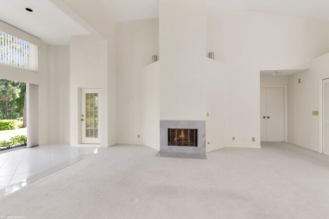 unfurnished living room with high vaulted ceiling, a fireplace, light carpet, and a wealth of natural light