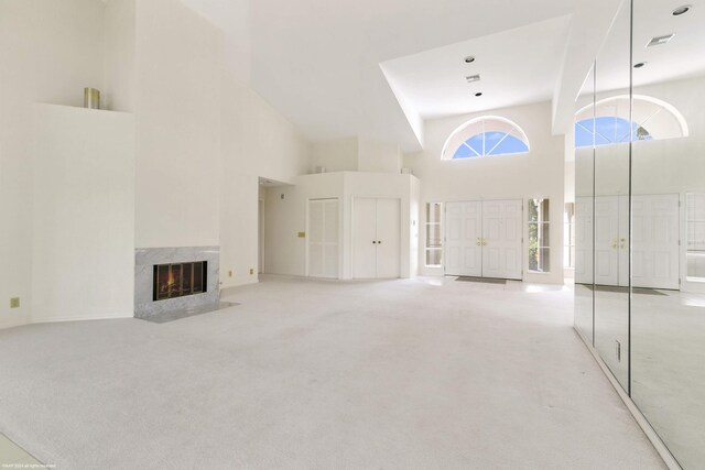 unfurnished living room featuring light carpet, a towering ceiling, and a high end fireplace