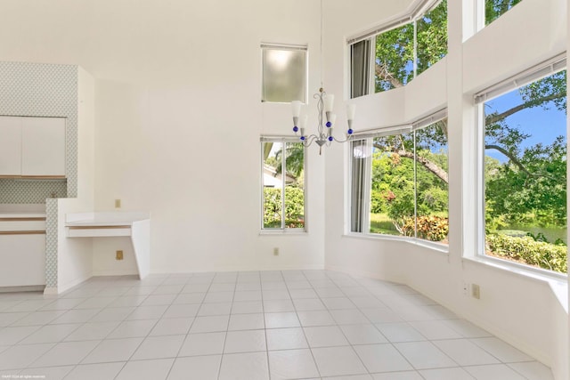 unfurnished living room with light tile patterned floors, a chandelier, and a high ceiling