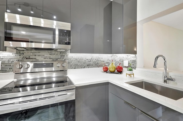 kitchen with appliances with stainless steel finishes, sink, gray cabinetry, backsplash, and light stone countertops