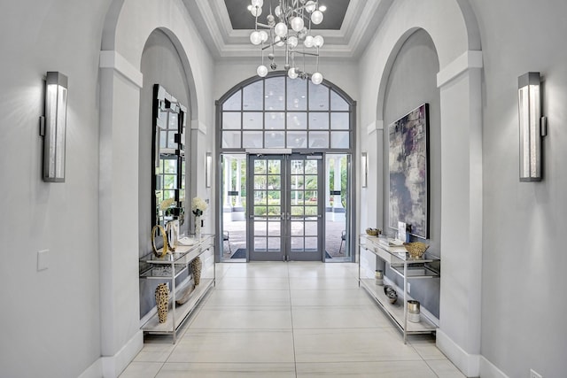 foyer entrance featuring light tile patterned floors, an inviting chandelier, a high ceiling, french doors, and a raised ceiling