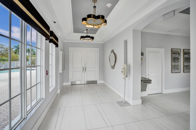 tiled entrance foyer featuring ornamental molding, a tray ceiling, and a chandelier