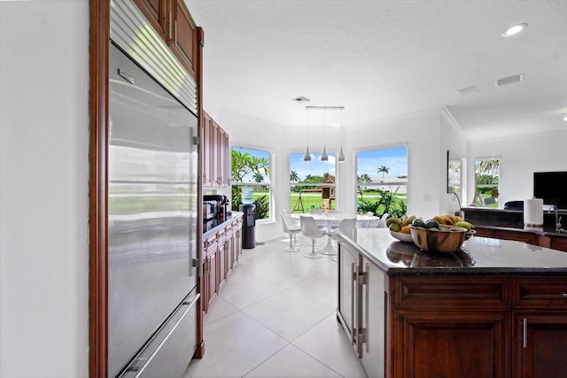 kitchen with a center island, light tile patterned floors, ornamental molding, built in fridge, and pendant lighting