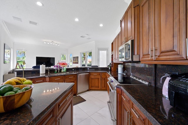 kitchen with sink, backsplash, dark stone counters, light tile patterned floors, and stainless steel appliances