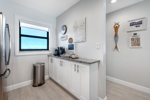 kitchen featuring stainless steel fridge, white cabinetry, light stone counters, and light hardwood / wood-style flooring