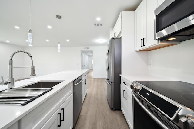 kitchen with stainless steel appliances, white cabinets, sink, pendant lighting, and light hardwood / wood-style floors