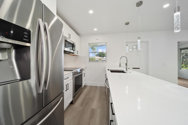 kitchen featuring decorative light fixtures, white cabinetry, stainless steel appliances, sink, and light hardwood / wood-style flooring