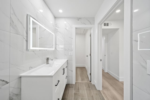 bathroom featuring tile walls, hardwood / wood-style floors, and dual bowl vanity