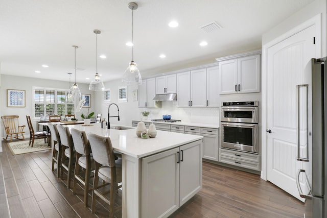 kitchen with pendant lighting, sink, dark wood-type flooring, a kitchen island with sink, and stainless steel appliances