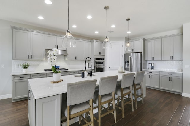 kitchen featuring stainless steel appliances, sink, a center island with sink, and decorative light fixtures