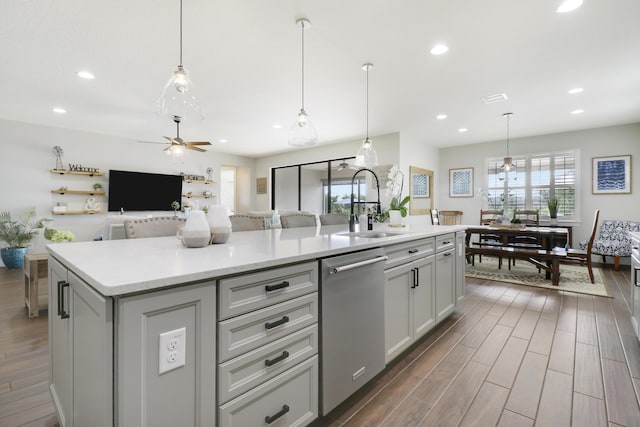 kitchen with gray cabinetry, decorative light fixtures, stainless steel dishwasher, and an island with sink