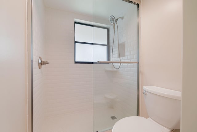 bathroom featuring a shower with door and toilet