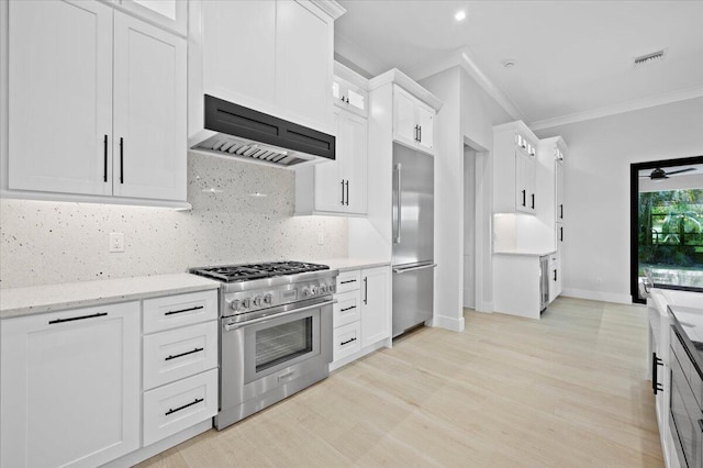 kitchen with custom exhaust hood, light stone counters, crown molding, premium appliances, and white cabinets