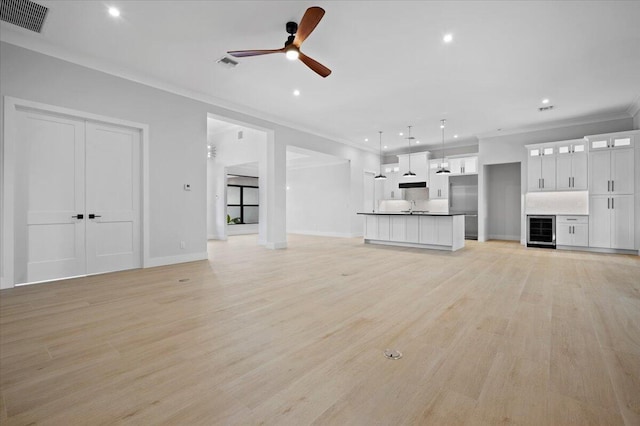 unfurnished living room with sink, beverage cooler, ceiling fan, crown molding, and light wood-type flooring