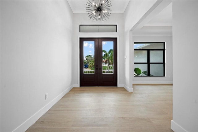 entrance foyer featuring ornamental molding, a notable chandelier, light hardwood / wood-style floors, and french doors