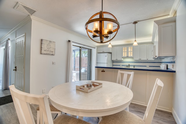 dining room with light hardwood / wood-style floors, crown molding, and an inviting chandelier