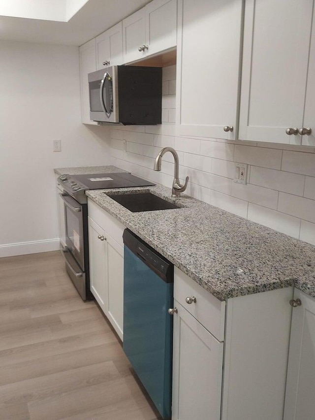 kitchen featuring light stone countertops, sink, stainless steel appliances, white cabinets, and light wood-type flooring