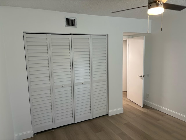 unfurnished bedroom with a closet, a textured ceiling, hardwood / wood-style flooring, and ceiling fan