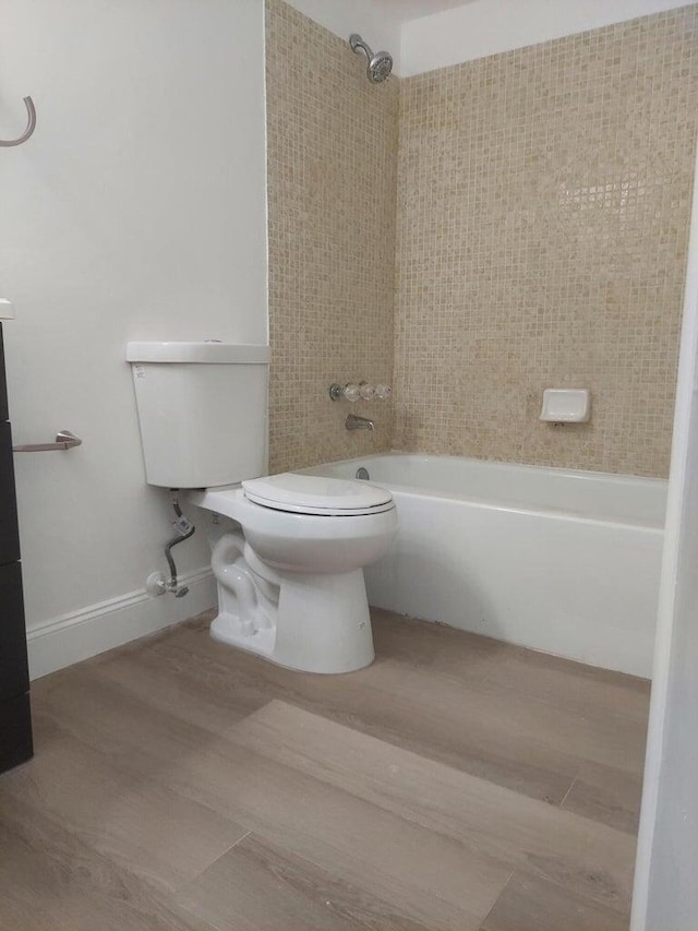 bathroom featuring wood-type flooring, tiled shower / bath combo, and toilet