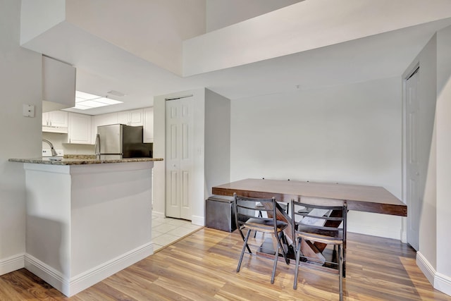 kitchen with dark stone counters, white cabinets, stainless steel fridge, light hardwood / wood-style floors, and kitchen peninsula