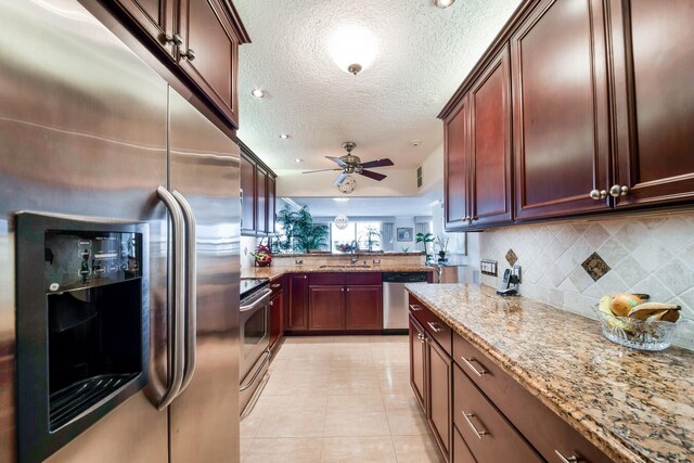 kitchen with light stone counters, a textured ceiling, stainless steel appliances, backsplash, and ceiling fan