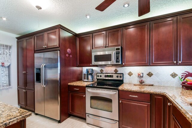 kitchen featuring a textured ceiling, ceiling fan, stainless steel appliances, and light stone counters