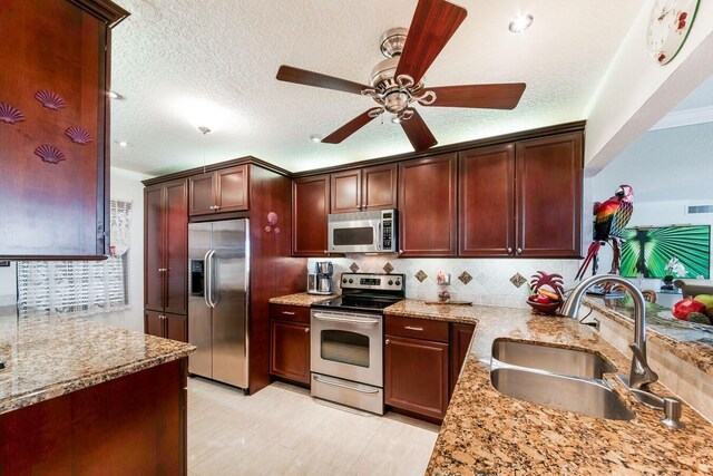 kitchen with light stone counters, a textured ceiling, sink, stainless steel appliances, and ceiling fan