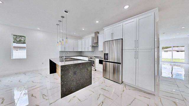 kitchen featuring a center island with sink, stainless steel fridge, light tile patterned floors, and plenty of natural light