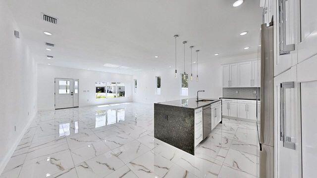 kitchen featuring white cabinetry, light tile patterned floors, a kitchen island with sink, decorative light fixtures, and sink