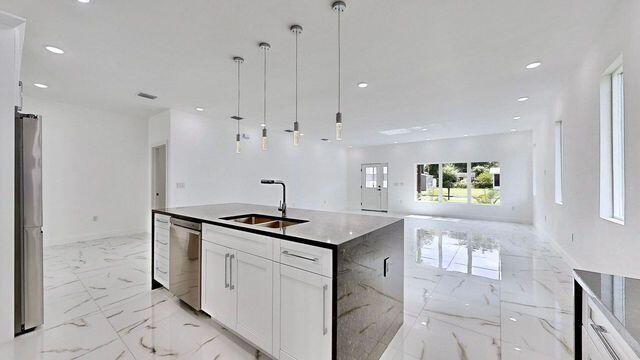 kitchen featuring appliances with stainless steel finishes, sink, light tile patterned floors, an island with sink, and white cabinetry