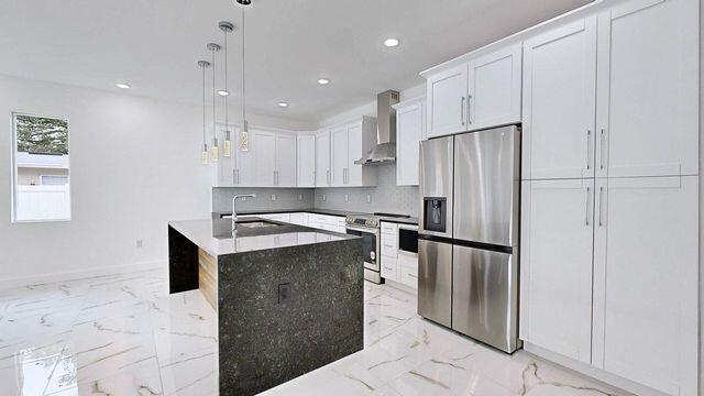 kitchen with stainless steel appliances, wall chimney range hood, sink, pendant lighting, and light tile patterned floors