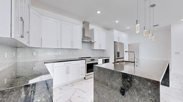 kitchen with light tile patterned flooring, wall chimney range hood, an island with sink, hanging light fixtures, and appliances with stainless steel finishes