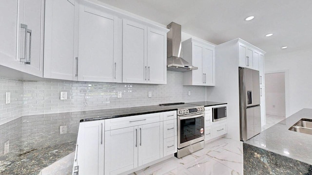 kitchen featuring white cabinetry, tasteful backsplash, wall chimney range hood, dark stone counters, and stainless steel appliances