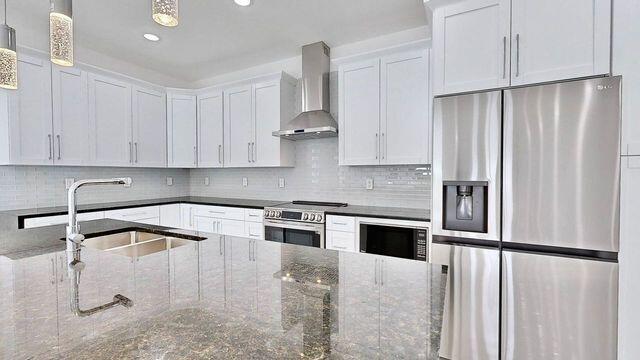 kitchen with stainless steel appliances, tasteful backsplash, wall chimney exhaust hood, and pendant lighting