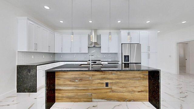 kitchen featuring stainless steel fridge with ice dispenser, wall chimney exhaust hood, light tile patterned floors, and white cabinets