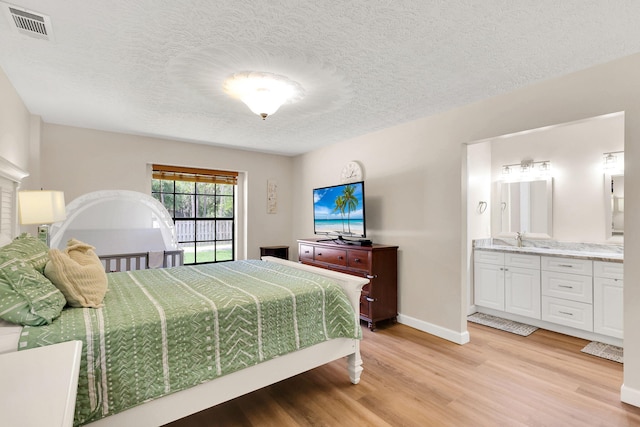 bedroom featuring connected bathroom, sink, a textured ceiling, and light wood-type flooring