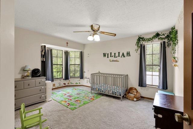 carpeted bedroom featuring a textured ceiling, a nursery area, and ceiling fan