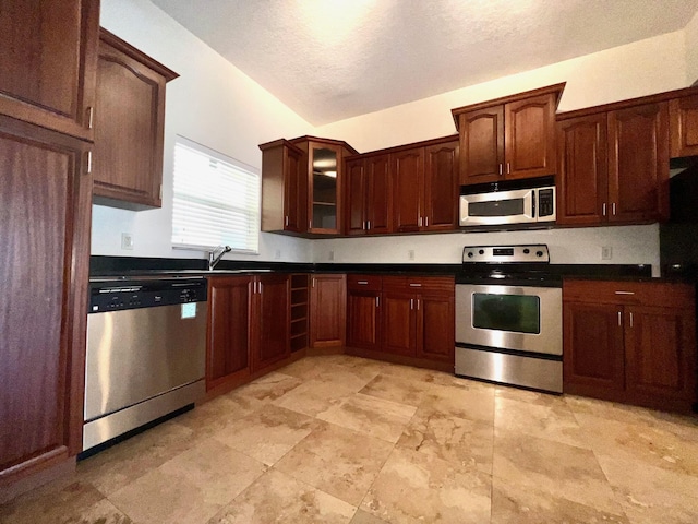 kitchen with glass insert cabinets, dark countertops, appliances with stainless steel finishes, and a sink