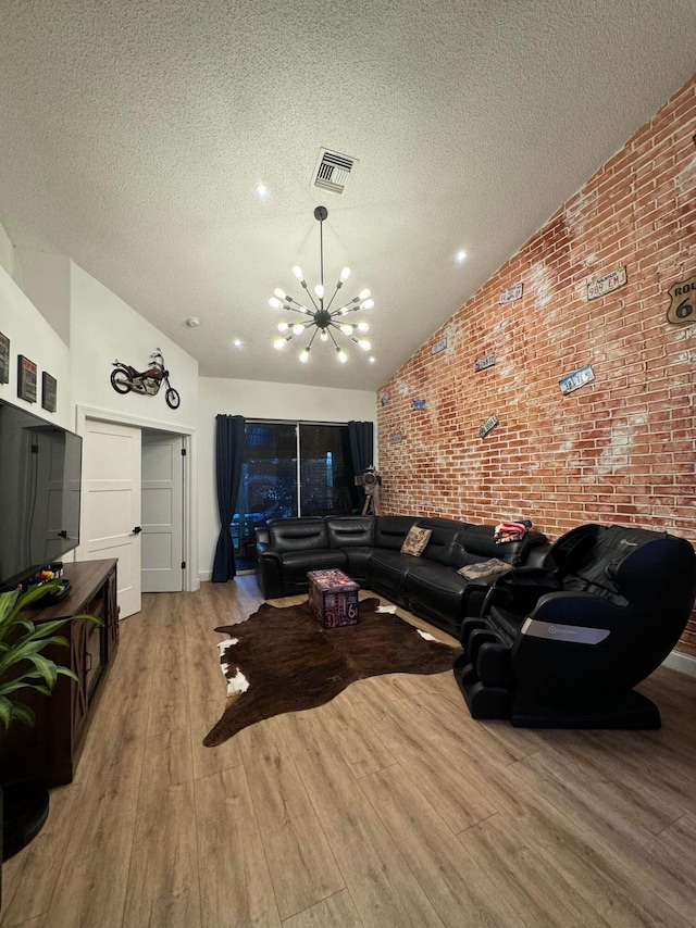 living room featuring lofted ceiling, a textured ceiling, an inviting chandelier, brick wall, and wood-type flooring