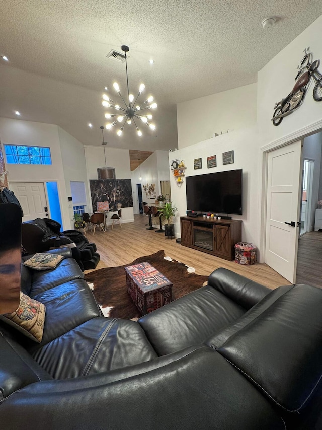 living room featuring high vaulted ceiling, a chandelier, a textured ceiling, and light hardwood / wood-style floors