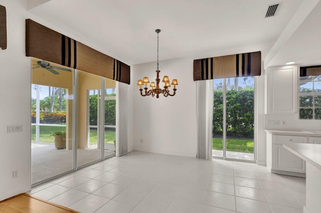 unfurnished dining area with light tile patterned flooring, ceiling fan with notable chandelier, and plenty of natural light