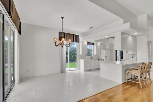 kitchen with white cabinetry, white fridge with ice dispenser, pendant lighting, light hardwood / wood-style floors, and a kitchen breakfast bar