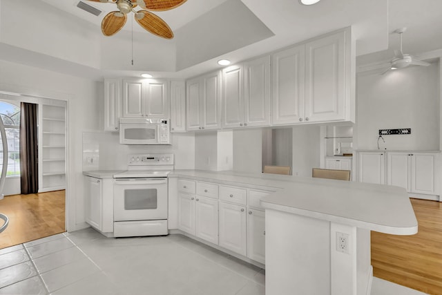 kitchen featuring a peninsula, white appliances, a ceiling fan, light countertops, and a tray ceiling