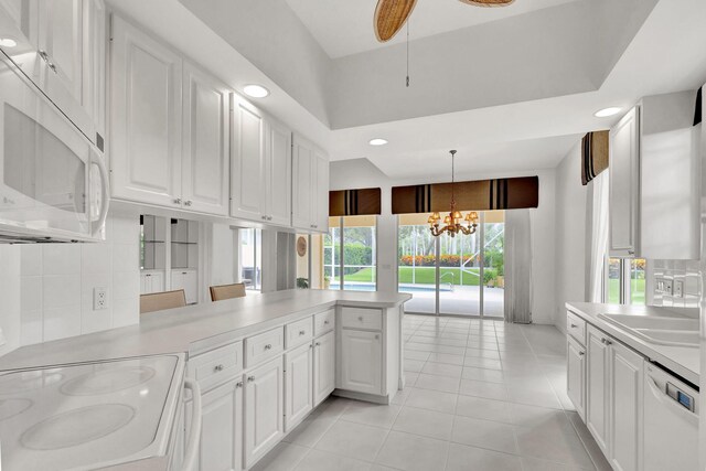 kitchen with a peninsula, white appliances, white cabinetry, and light countertops