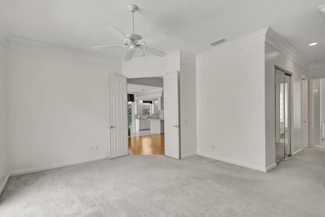 empty room featuring light colored carpet, visible vents, ornamental molding, a ceiling fan, and baseboards