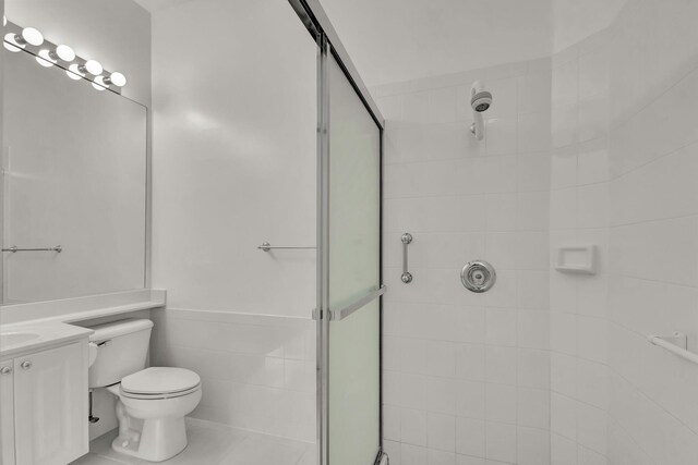 full bathroom featuring a stall shower, wainscoting, toilet, vanity, and tile walls