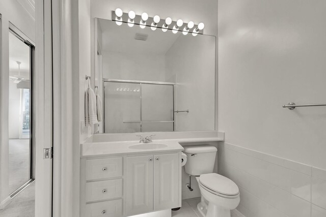 full bathroom featuring a wainscoted wall, tile walls, toilet, an enclosed shower, and vanity