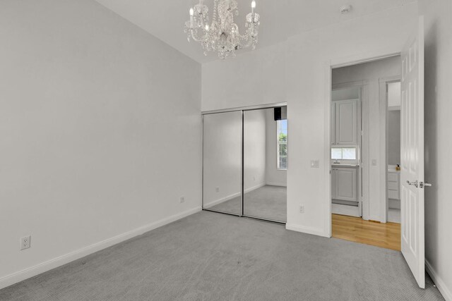 unfurnished bedroom with carpet floors, a closet, an inviting chandelier, and baseboards