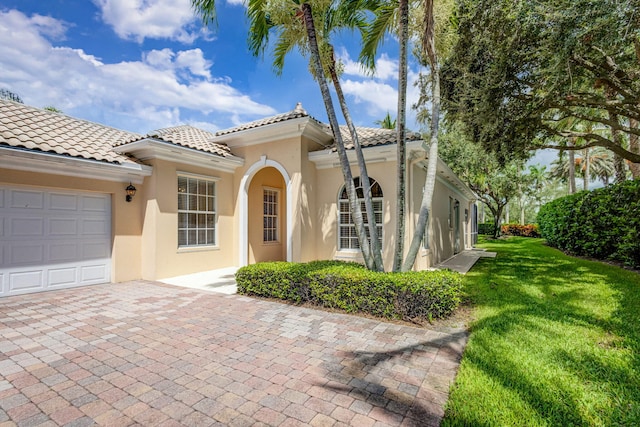 mediterranean / spanish house with a front yard, a tiled roof, an attached garage, and stucco siding