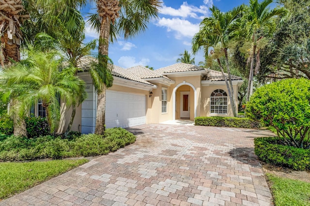 mediterranean / spanish house with a garage, a tiled roof, decorative driveway, and stucco siding